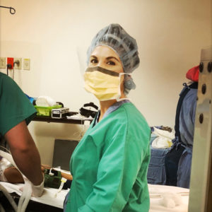 Surgeon in scrubs and mask, focused on patient care in a surgical setting.