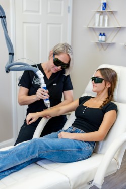 Aesthetician Judit in black scrubs performing a laser skin treatment on a patient's arm at Lentz Plastic Surgery & Medical Spa.