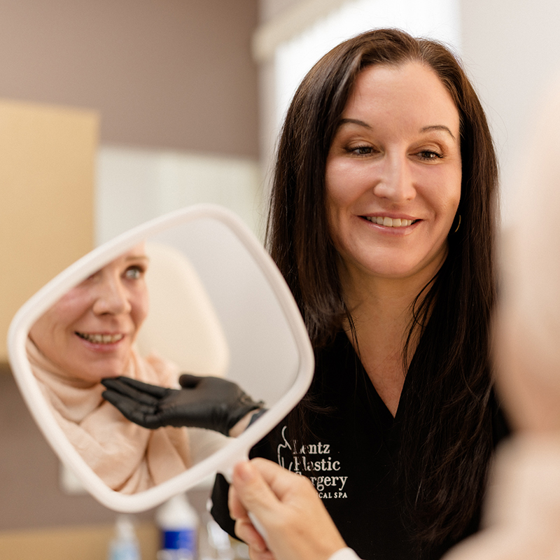 Aesthetic provider at Lentz Plastic Surgery & Medical Spa holding a mirror for a patient to review their facial treatment results.