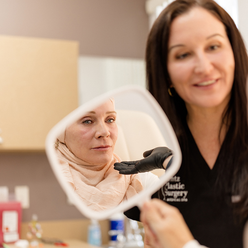 Professional aesthetician at Lentz Plastic Surgery & Medical Spa holding a mirror for a patient to review their clinical results.